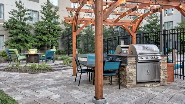 An outdoor patio area with a wooden pergola, a grill, and seating. - Homewood Suites by Hilton Leesburg (Leesburg)
