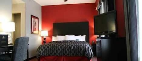 A hotel room with a bed, a desk, a chair, a television, and a ceiling fan.