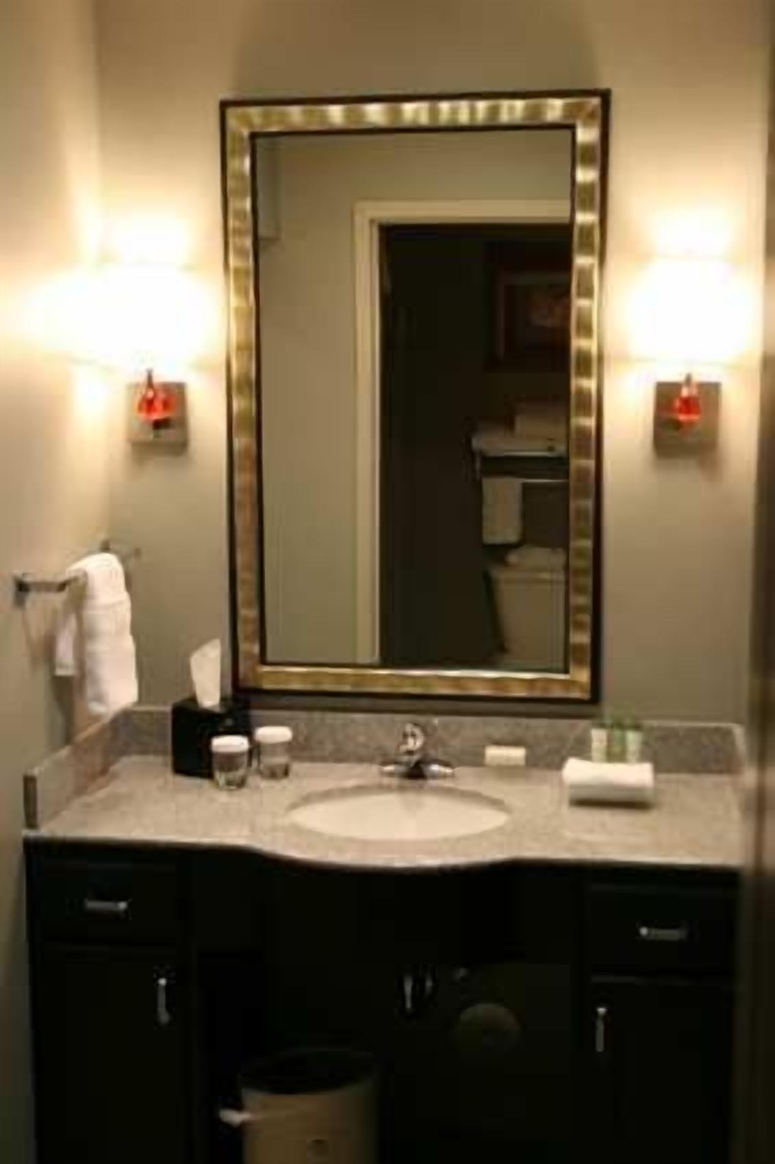 A bathroom with a large mirror, two wall-mounted lights, a sink, and a towel rack.