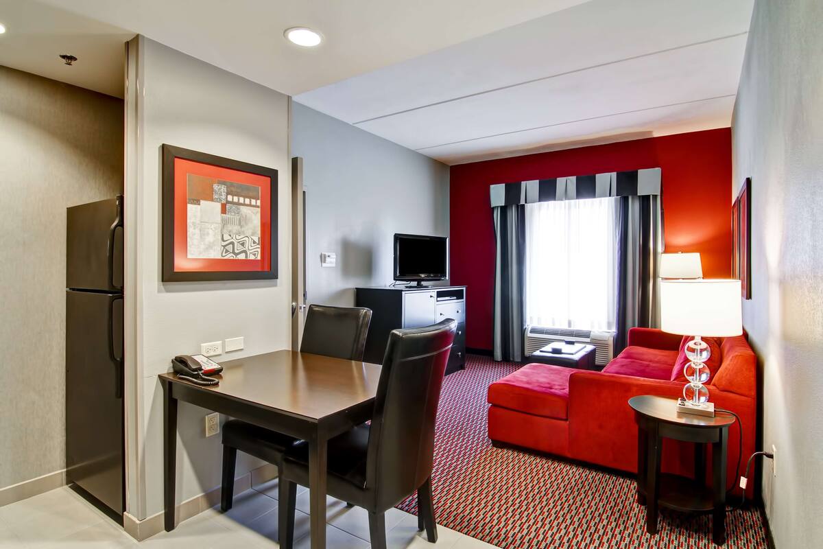 Een hotelkamer met een eethoek, een televisie, een rode bank en een lamp.