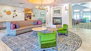 A lobby with a patterned sofa, green chairs, a fireplace, and a large chandelier. - Homewood Suites by Hilton Leesburg (Leesburg)