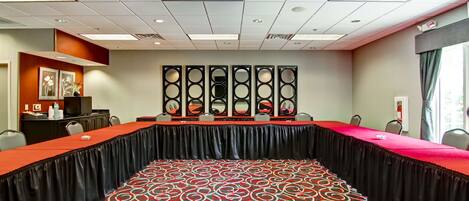 A conference room with a long table, chairs, a patterned carpet, a ceiling with recessed lighting, and a decorative wall panel.