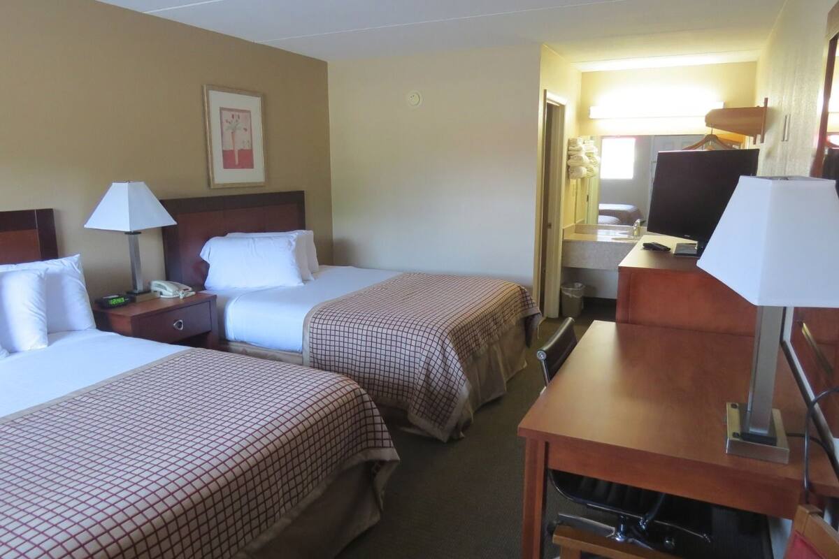 Une chambre d’hôtel avec deux lits, un bureau avec un ordinateur, une lampe et un tableau encadré au mur.