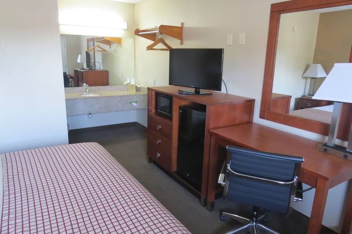 Une chambre d’hôtel comprenant un lit, un bureau avec une chaise, une télévision, un miroir et une commode.