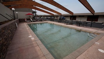 Una piscina con un muro de piedra en un lado y una zona techada con asientos en el otro.