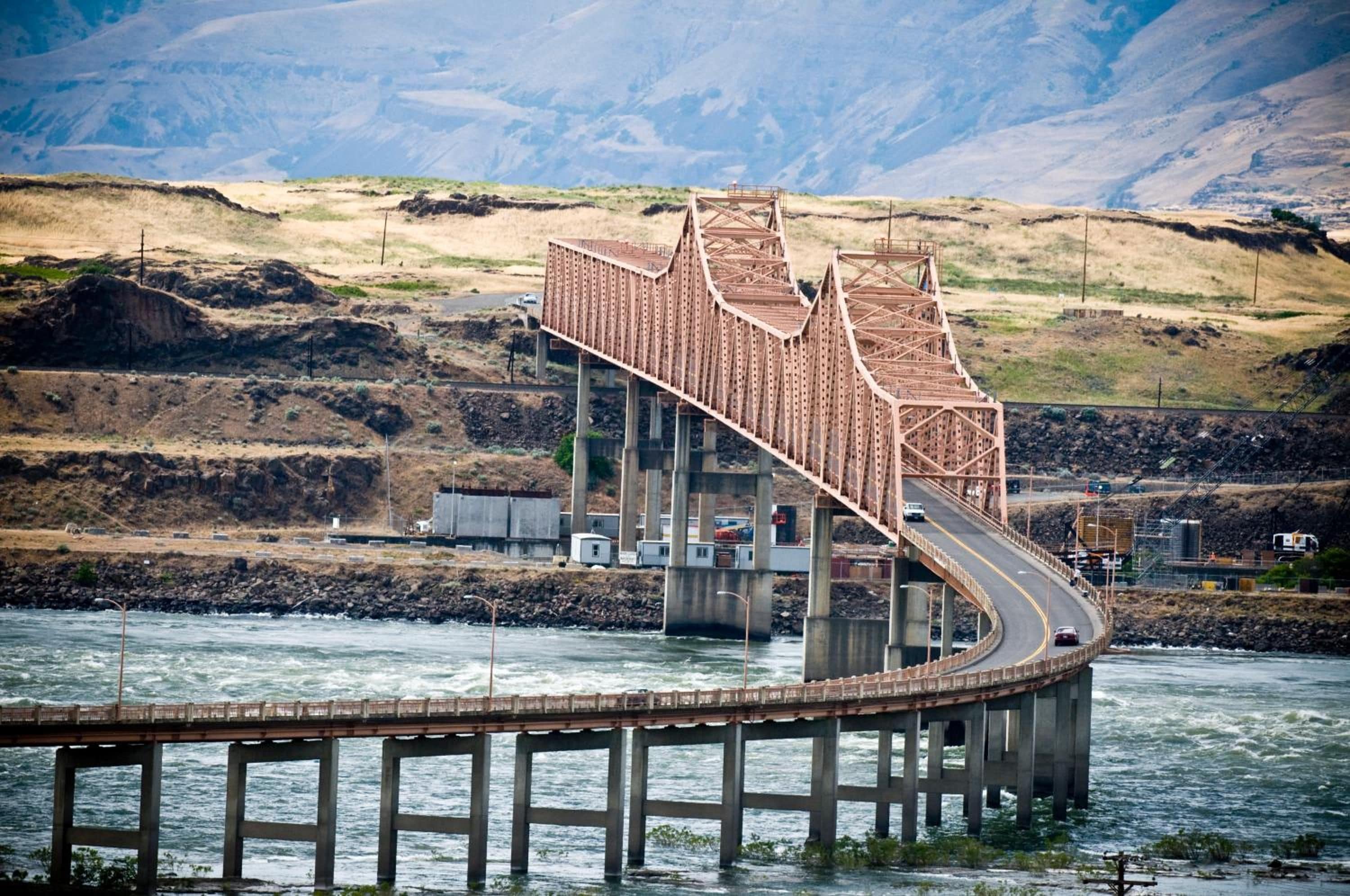 A bridge over a river with a mountainous backdrop.