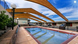 A swimming pool with a wooden deck and lounge chairs, surrounded by a building with a metal fence. - Celilo Inn (The Dalles)