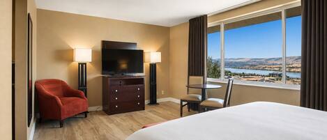 A hotel room with a bed, a TV, a desk, and a view of a landscape.