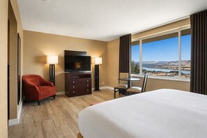 A hotel room with a bed, a TV, a desk, and a view of a landscape.