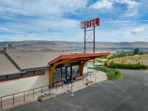Um motel com toldo vermelho, área de estar externa e vista para colinas ao fundo.