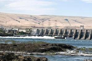 Uma barragem com água a correr, rodeada por terreno rochoso e colinas.