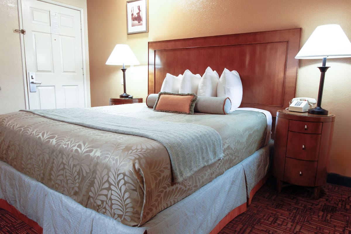 A hotel room with a large bed, two bedside tables, a wooden headboard, and a door.