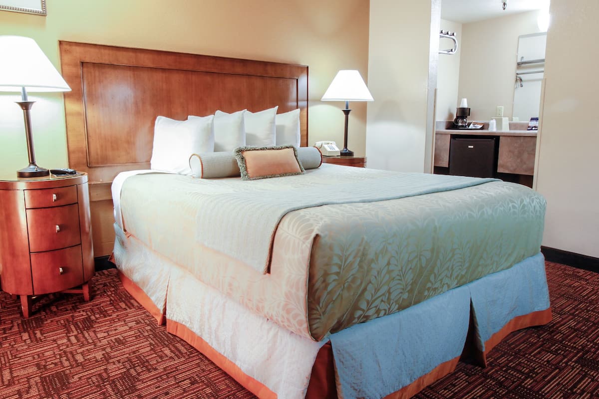 A hotel room with a large bed, two bedside tables with lamps, a wooden headboard, a small desk with a telephone, and a bathroom visible through an open door.