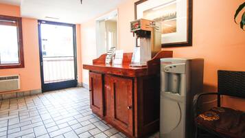 A reception area with a wooden counter, a coffee machine, a refrigerator, and a chair.