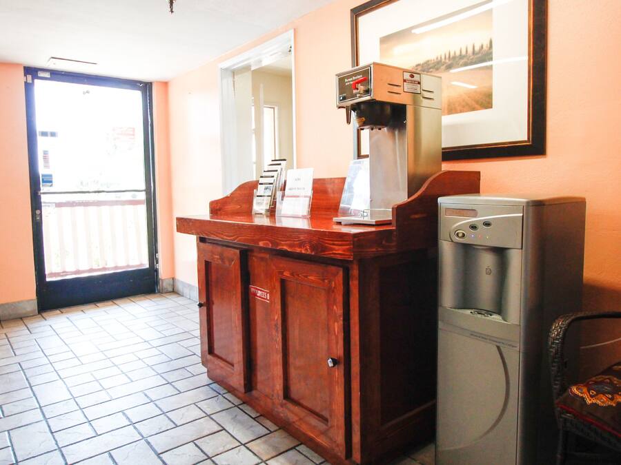 A reception area with a wooden counter, a coffee machine, a refrigerator, and a chair.