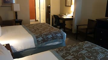 A hotel room with two beds, a desk, a chair, a TV, and a door leading to another room.