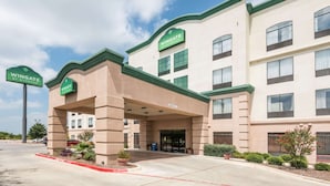Um hotel Wingate by Wyndham com fachada bege, detalhes verdes e entrada coberta.