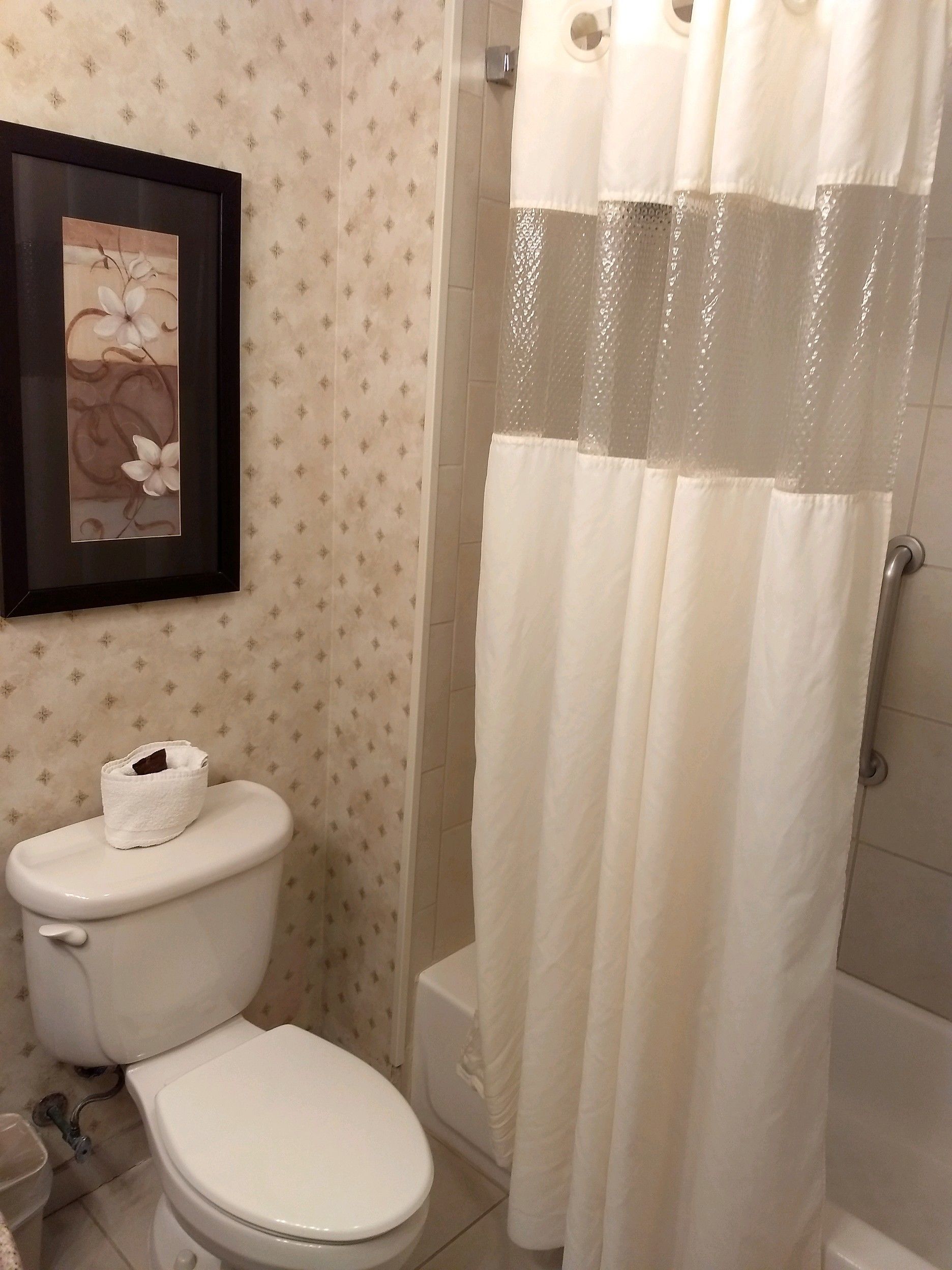 Un baño con inodoro, una obra de arte floral enmarcadas en la pared y una cortina de ducha.