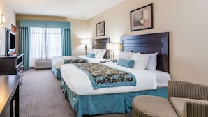 Quarto de hotel com duas camas, uma mesa, uma televisão e uma janela grande com cortinas.