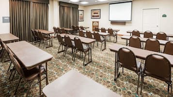Una sala de conferencias con mesas y sillas, una pantalla de proyector y suelo alfombrado.