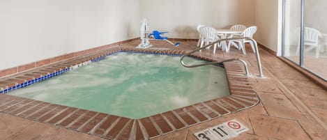 Ein Hallenbad mit Fliesenrand, einem blauen Stuhl und weißen Stühlen um einen Tisch.
