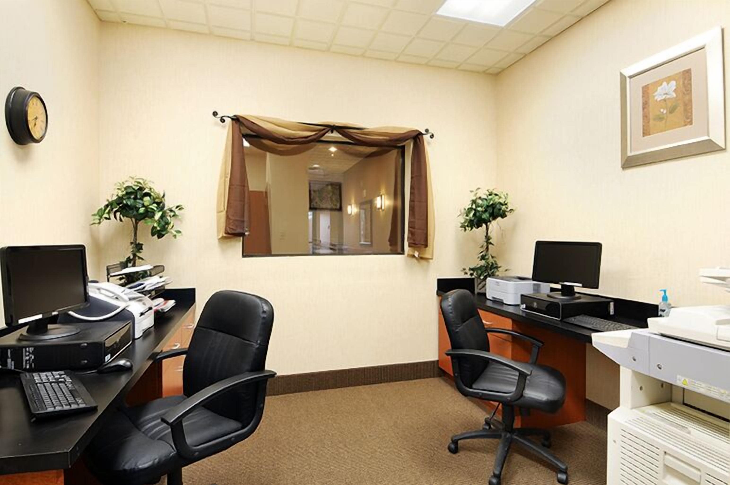 Un bureau avec deux tables de travail, des ordinateurs, des chaises, une horloge, un tableau encadré et une fenêtre avec des rideaux.