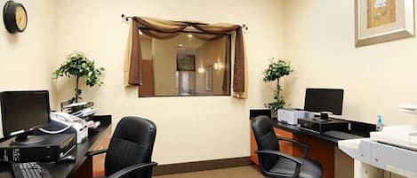 Un bureau avec deux tables de travail, des ordinateurs, des chaises, une horloge, un tableau encadré et une fenêtre avec des rideaux.