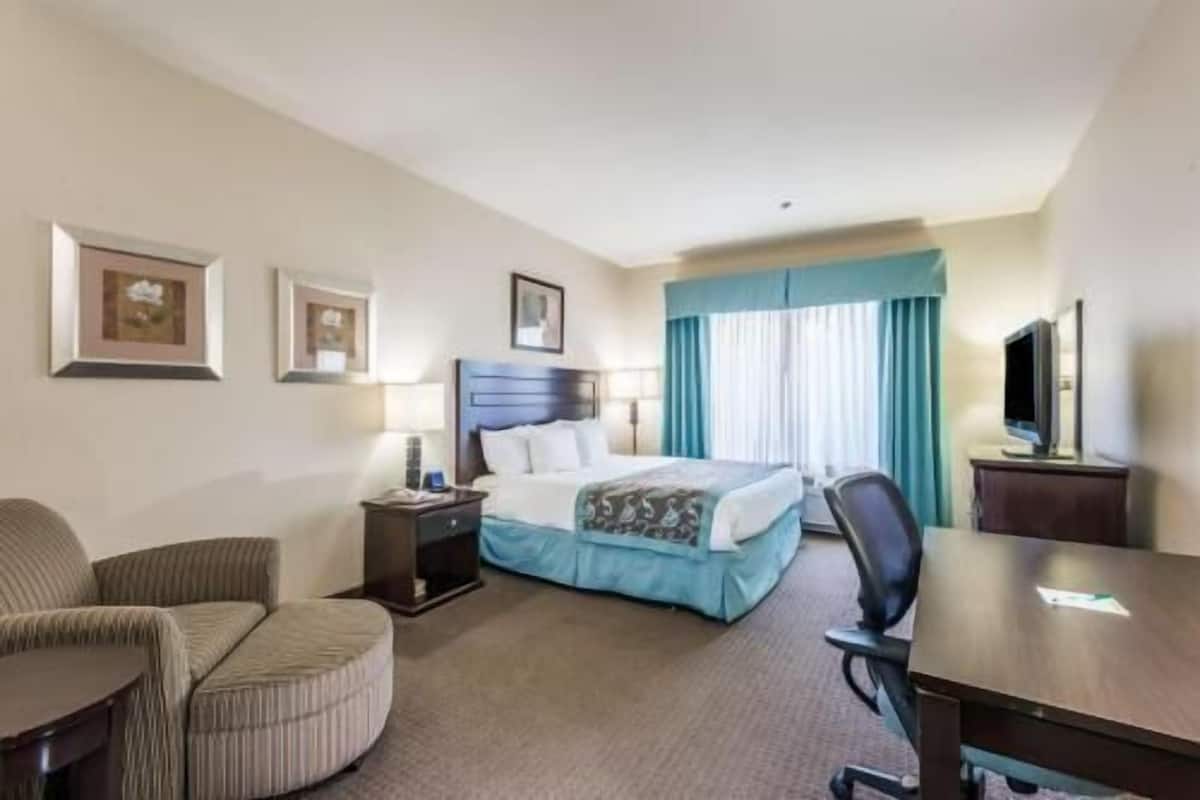 Une chambre d’hôtel avec un lit, un bureau, une chaise, une télévision et une fenêtre avec des rideaux.
