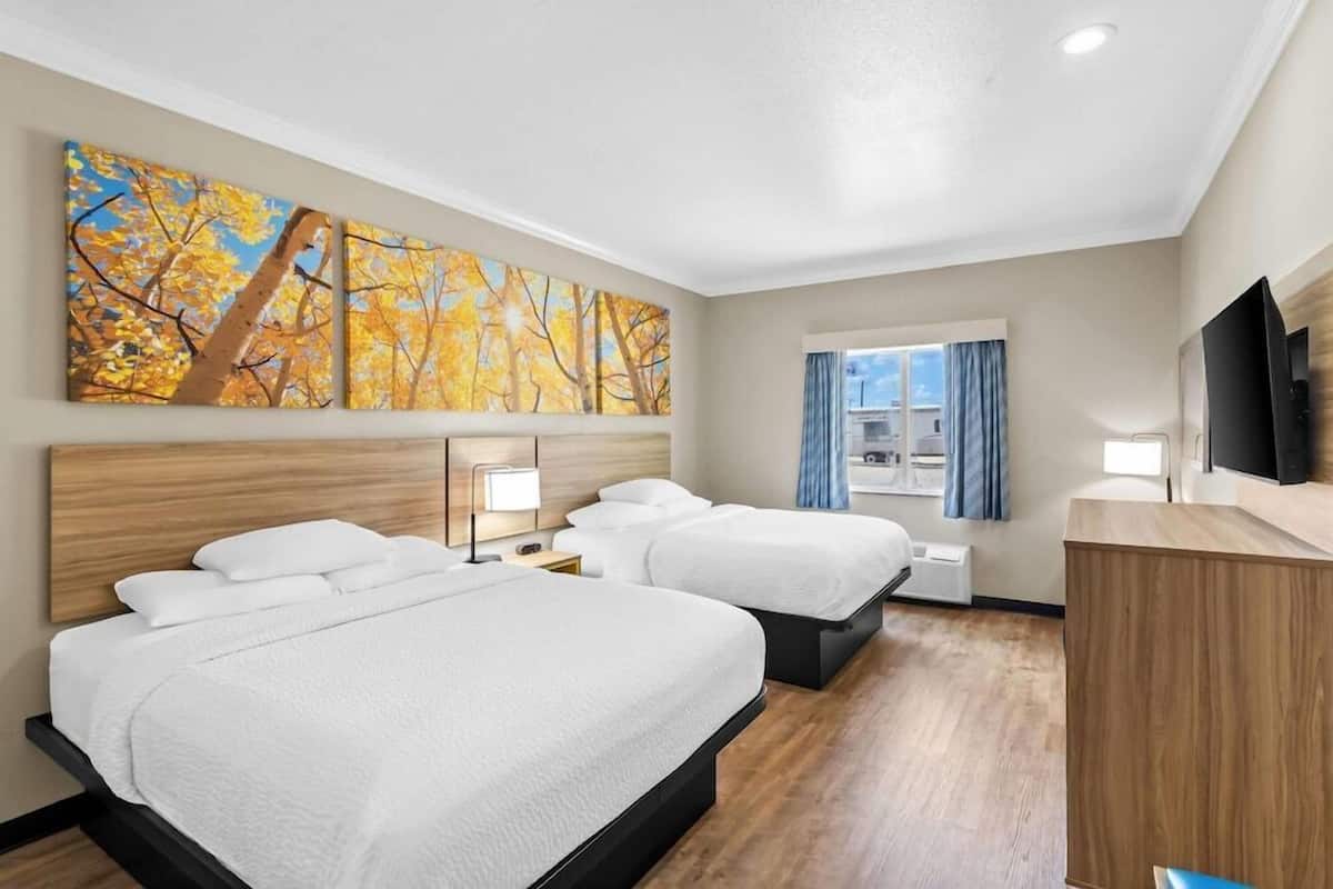 Ein Hotelzimmer mit zwei Betten, einem Fernseher, einem Schreibtisch und einem Vorhangfenster.
