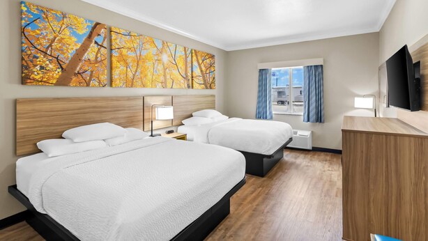 Habitación de hotel con dos camas, televisión, escritorio y obras de arte en la pared.