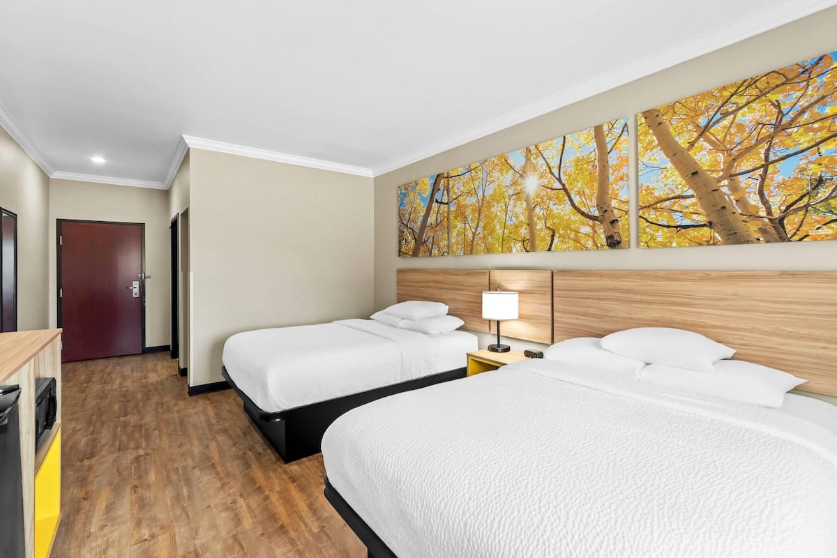 Ein Hotelzimmer mit zwei Betten, Holzboden, einem Gemälde von Herbstbäumen und einem hölzernen Bettgestell.
