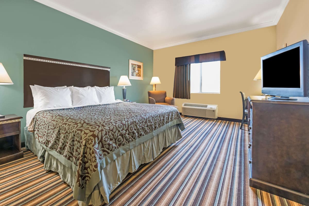Ein Hotelzimmer mit einem großen Bett, zwei Nachttischlampen, einem Fernseher, einem Schreibtisch und einem Fenster mit Vorhängen.
