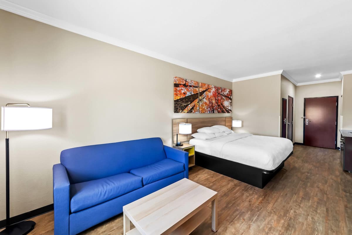 Ein Hotelzimmer mit einem blauen Sofa, einem Bett, Holzboden und einem Bild an der Wand.