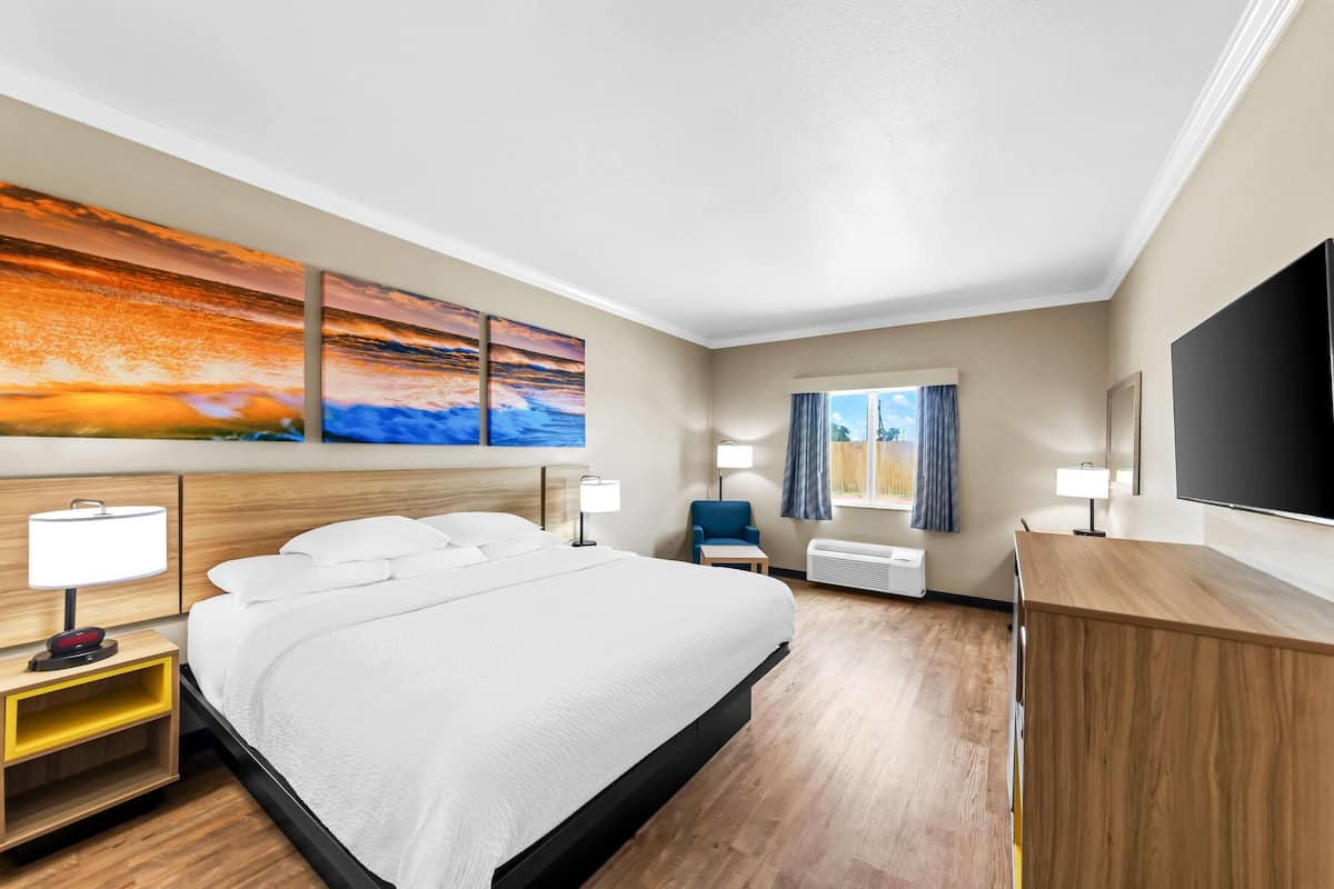 Ein Hotelzimmer mit einem großen Bett, Nachttischen mit Lampen, einem Flachbildfernseher, einem Schreibtisch und einem Fenster mit Vorhängen.