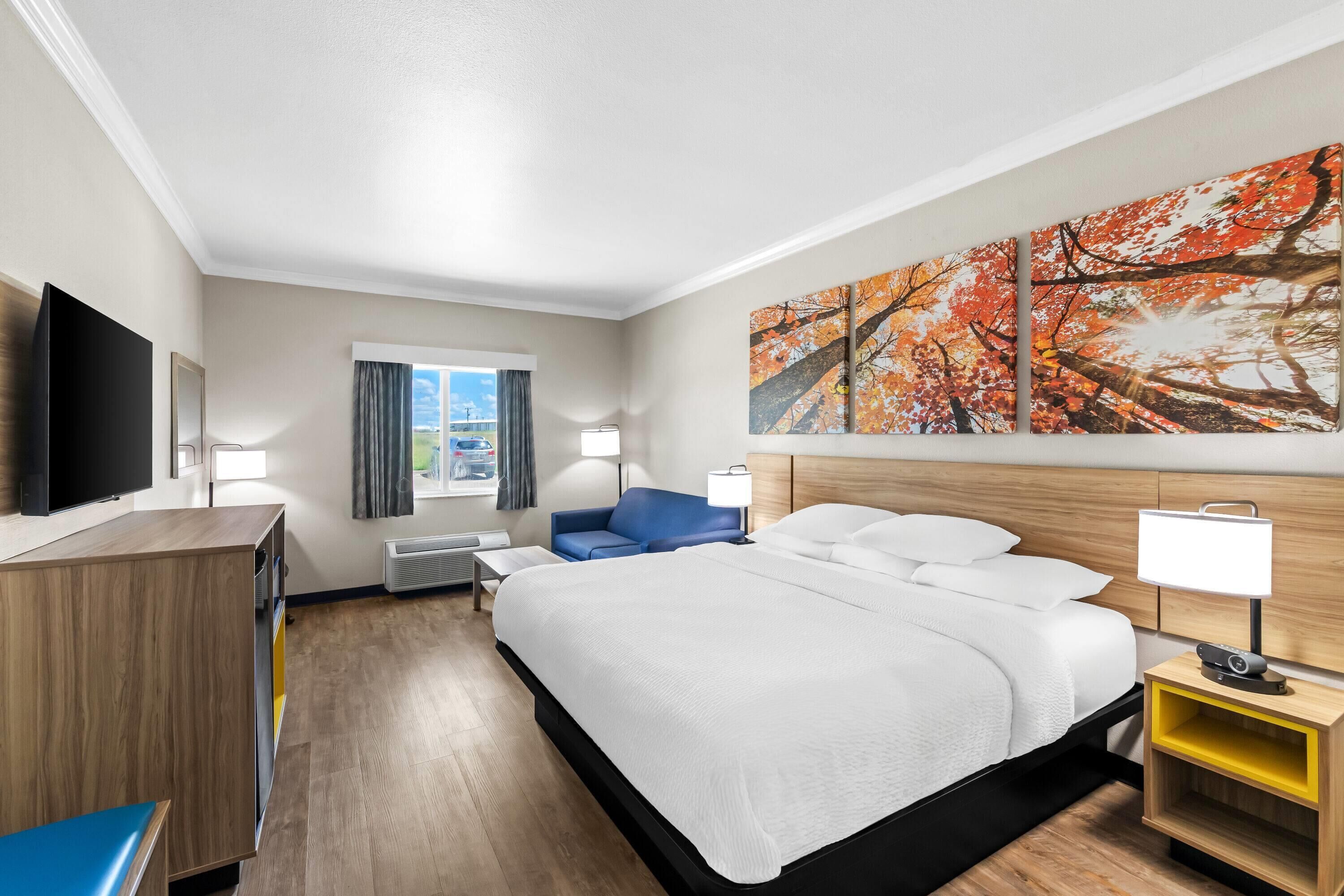 A hotel room with a large bed, a TV, a desk, and a painting on the wall.