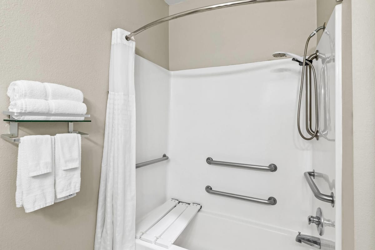 Ein modernes Badezimmer mit Dusche, Haltegriffen, einer Glasablage mit Handtüchern und einem weißen Duschvorhang.