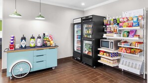 A vending area with coffee machines, a refrigerated display, and snack shelves. - Spark by Hilton Pearland (Pearland)