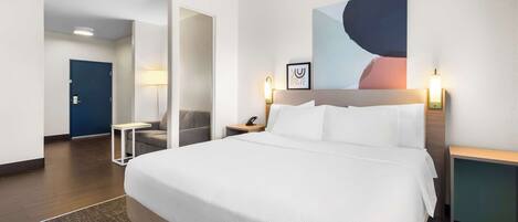 A hotel room with a large bed, a desk, a chair, and a door leading to another room.