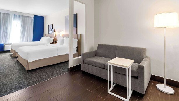 A hotel room with a bed, a sofa, a small table, and a floor lamp. - Spark by Hilton Pearland (Pearland)