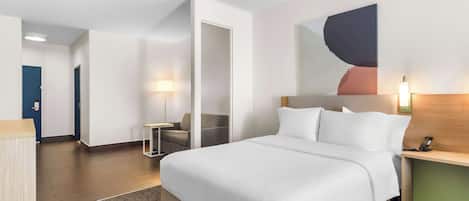 A hotel room with a large bed, a desk, a chair, and a wall-mounted lamp.