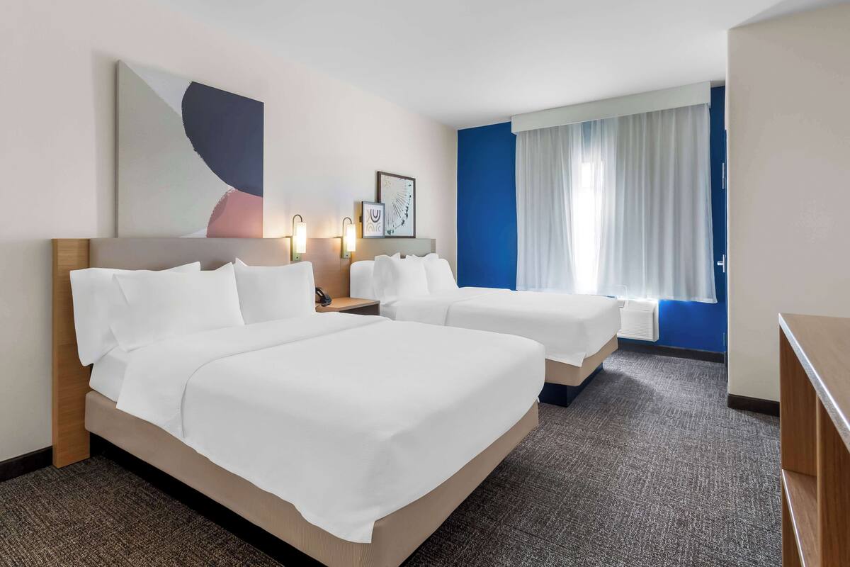 A hotel room with two beds, a large abstract painting, a framed picture, and a window with curtains.