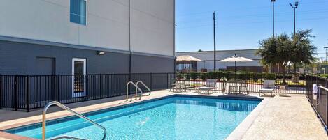 A rectangular swimming pool with a metal ladder, surrounded by a tiled deck and a black metal fence.