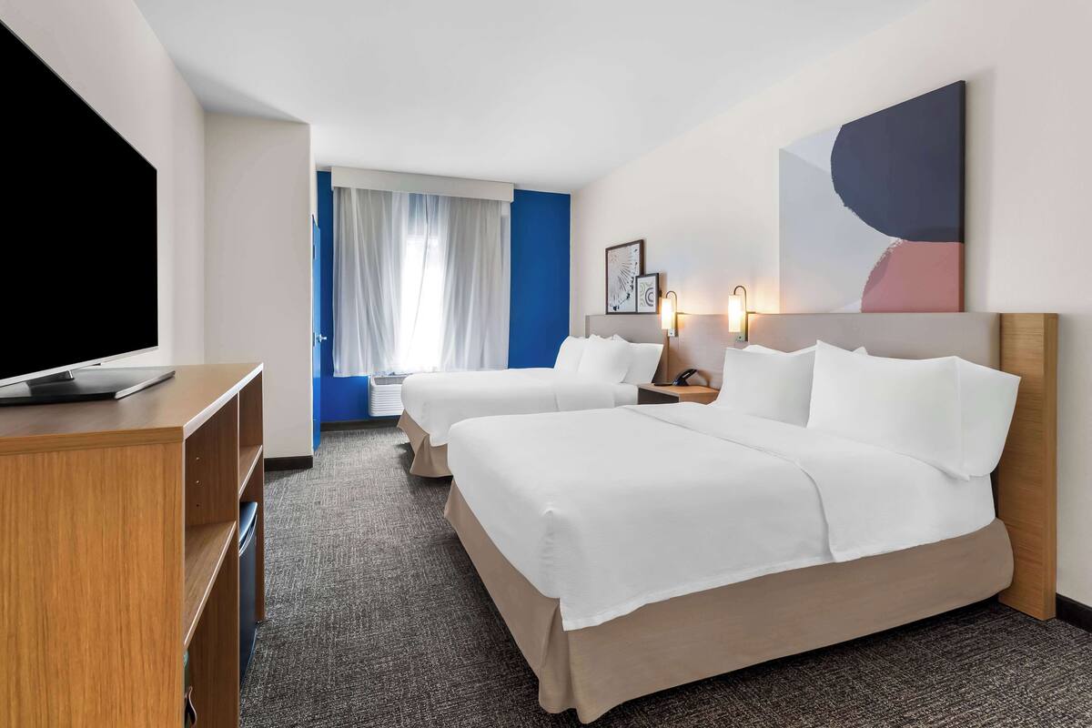 A hotel room with two beds, a desk, a TV, and a large abstract painting on the wall.