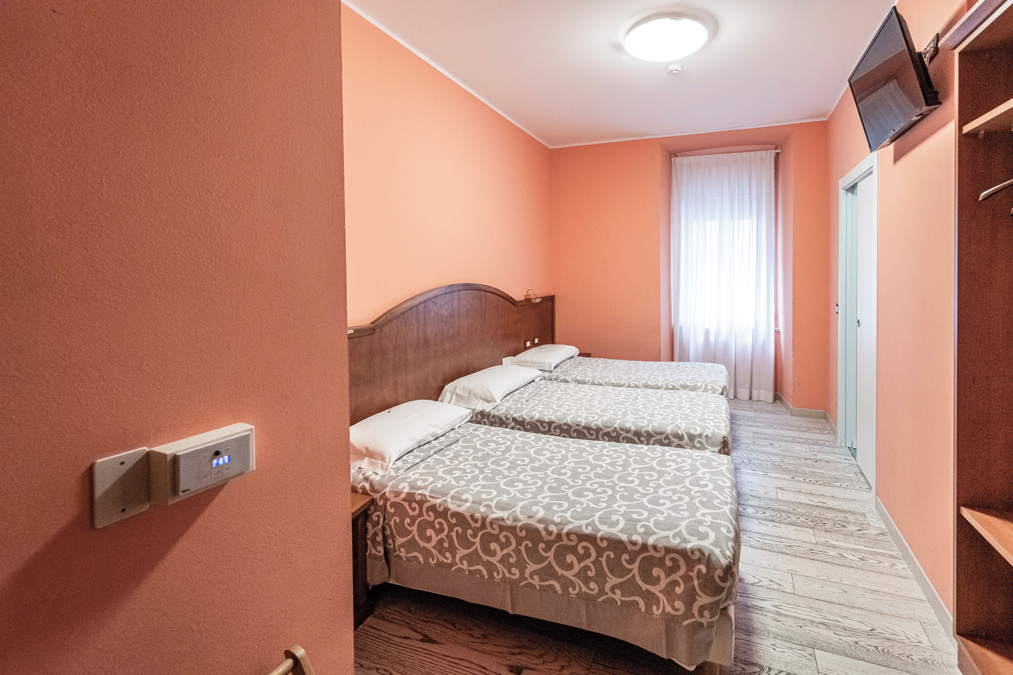 Ein Hotelzimmer mit zwei Betten, einem an der Wand befestigten Fernseher und einem Fenster mit Vorhängen.