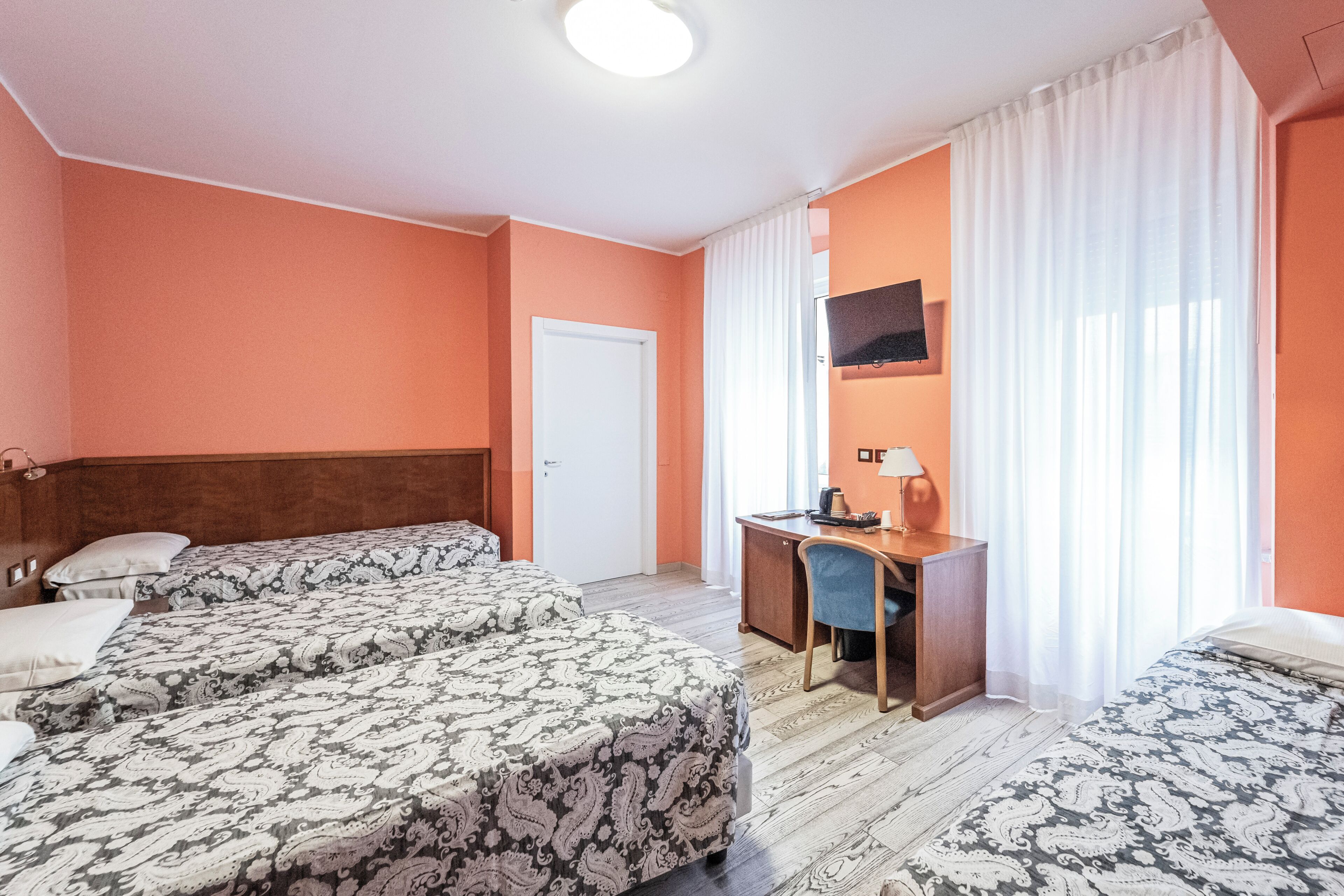 Une chambre d’hôtel avec deux lits, un bureau, une chaise, une télévision et une fenêtre avec des rideaux.