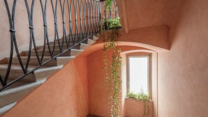 A staircase with a wrought iron railing, a curved wall, and a window with plants. - Hotel Italia (Trieste)