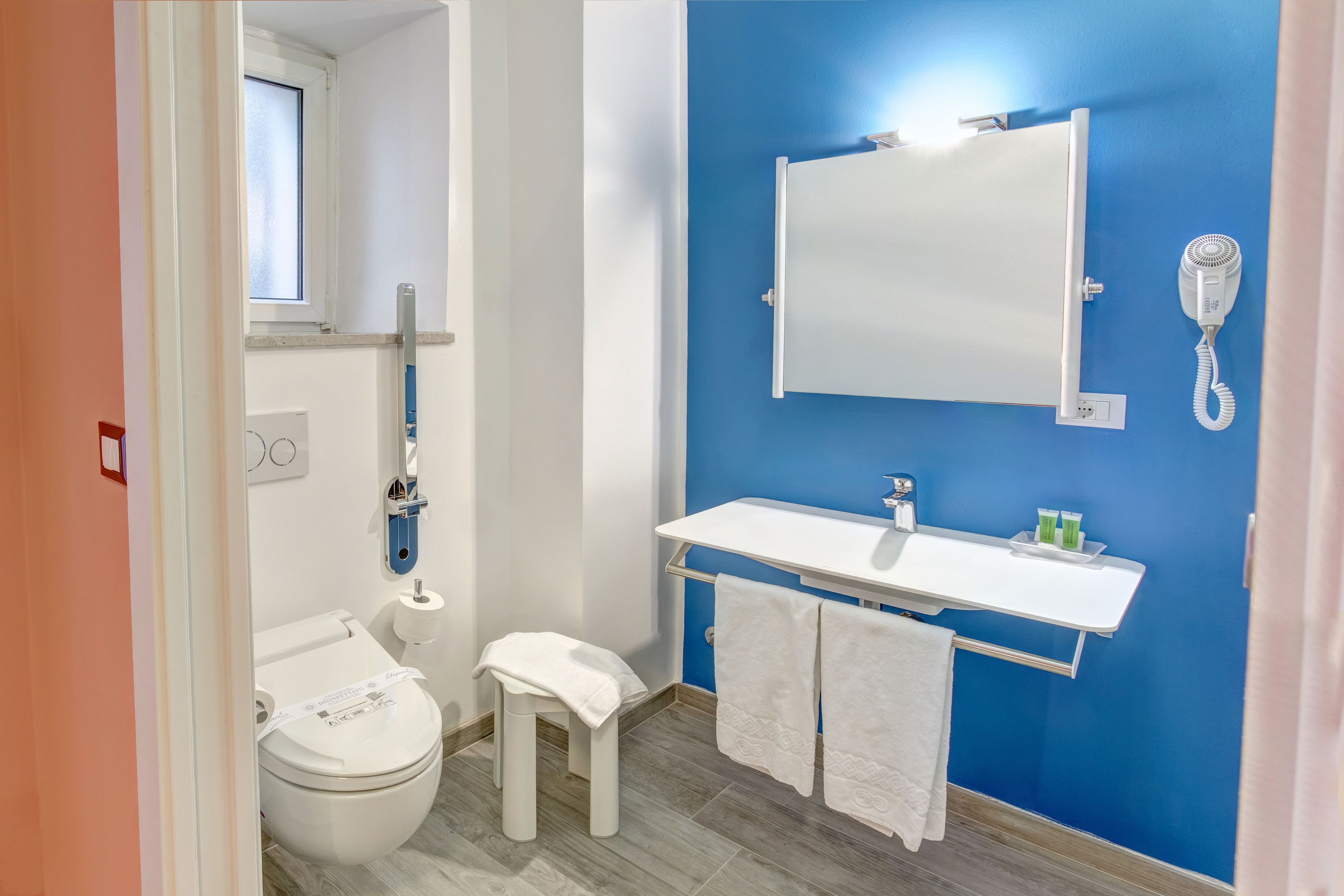 Ein Badezimmer mit Toilette, Waschbecken mit Spiegel, Föhn und Fenster.