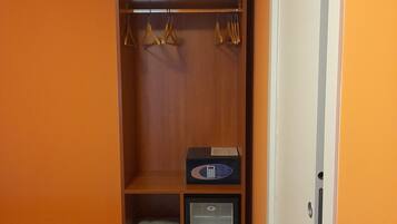 Un dormitorio con una pared naranja, un armario de madera, una cama con ropa de cama estampada y un refrigerador pequeño.