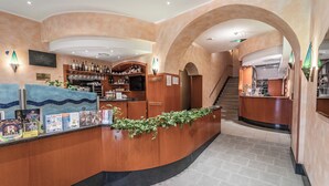 A reception area with a curved counter, a staircase, and a bar area with shelves of bottles. - Hotel Italia (Trieste)