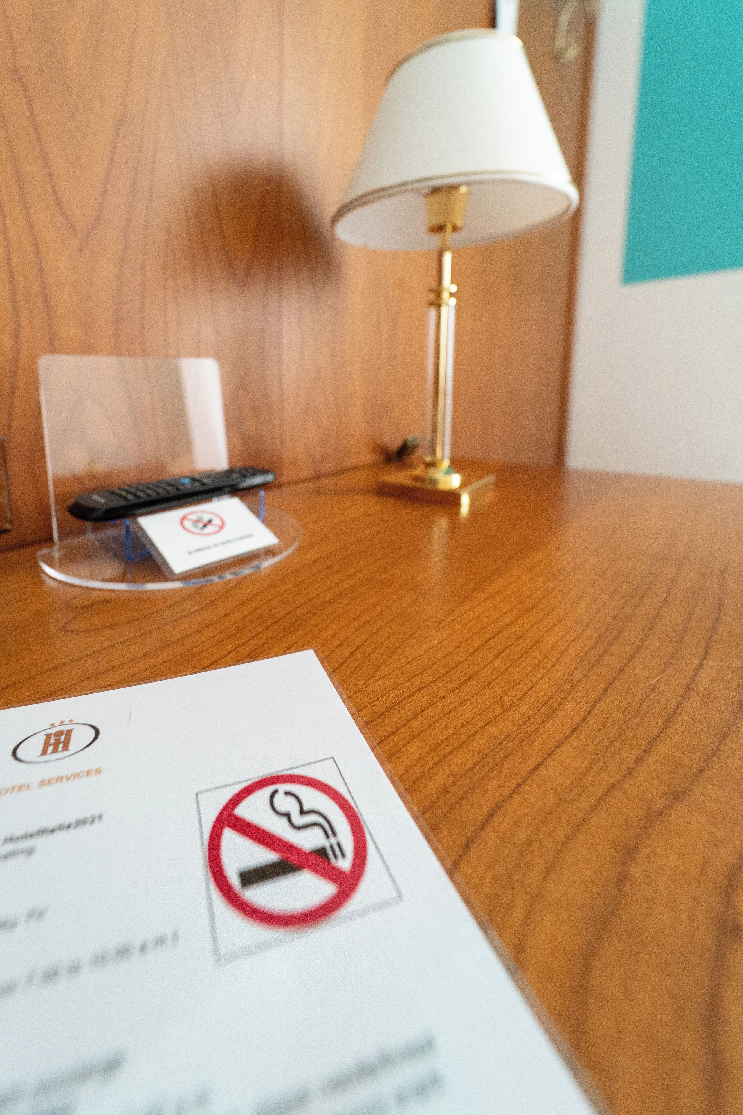 A wooden table with a remote control on a stand, a no-smoking sign, and a lamp.